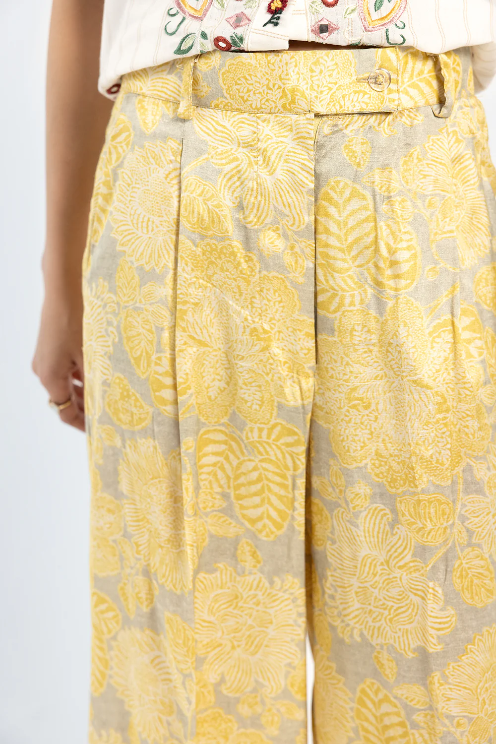 Close-up shot highlighting the vibrant floral print and fluid filament fabric of a contemporary yellow trouser.