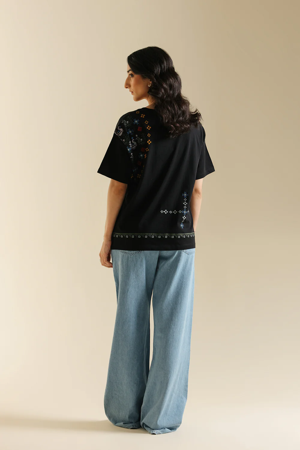 Back studio portrait of Biljiki jet black t-shirt featuring multi-colored geometric embroidery on a 5'6 model.