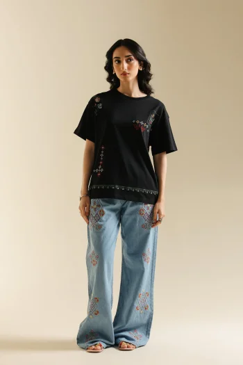 Front studio portrait of Biljiki jet black t-shirt featuring multi-colored geometric embroidery on a 5'6 model.
