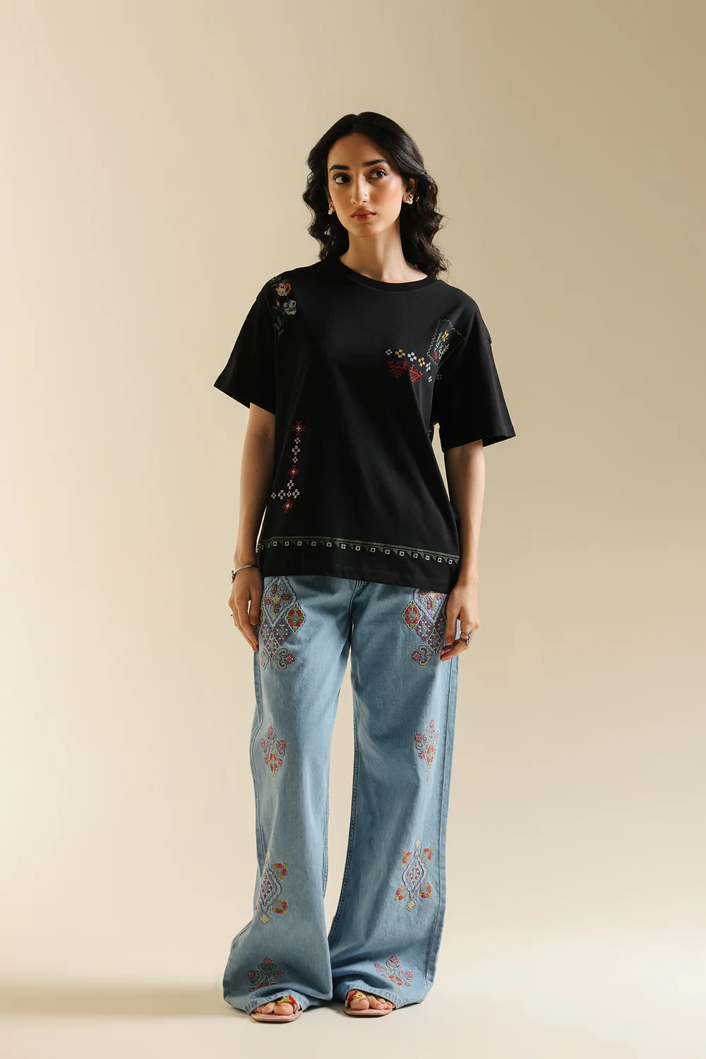 Front studio portrait of Biljiki jet black t-shirt featuring multi-colored geometric embroidery on a 5'6 model.