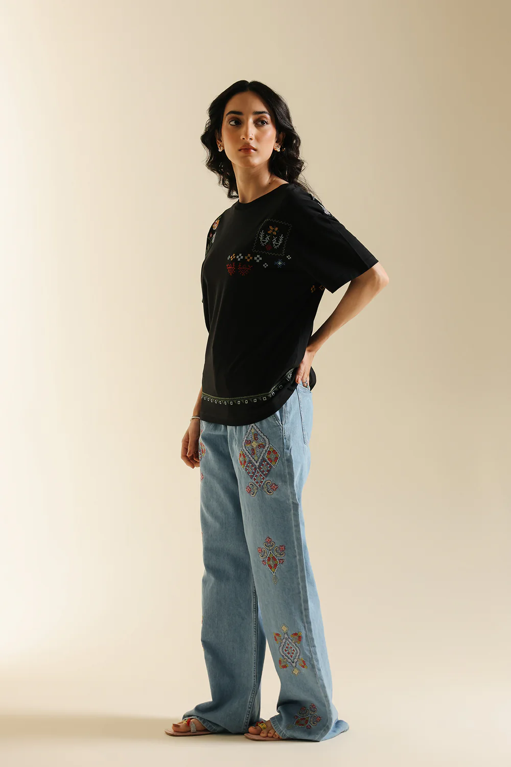 Side studio portrait of Biljiki jet black t-shirt featuring multi-colored geometric embroidery on a 5'6 model.