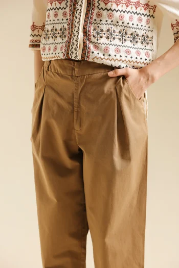Close-up shot highlighting the precise subtle front pleating and structural drape of the premium light khaki tailored trousers.