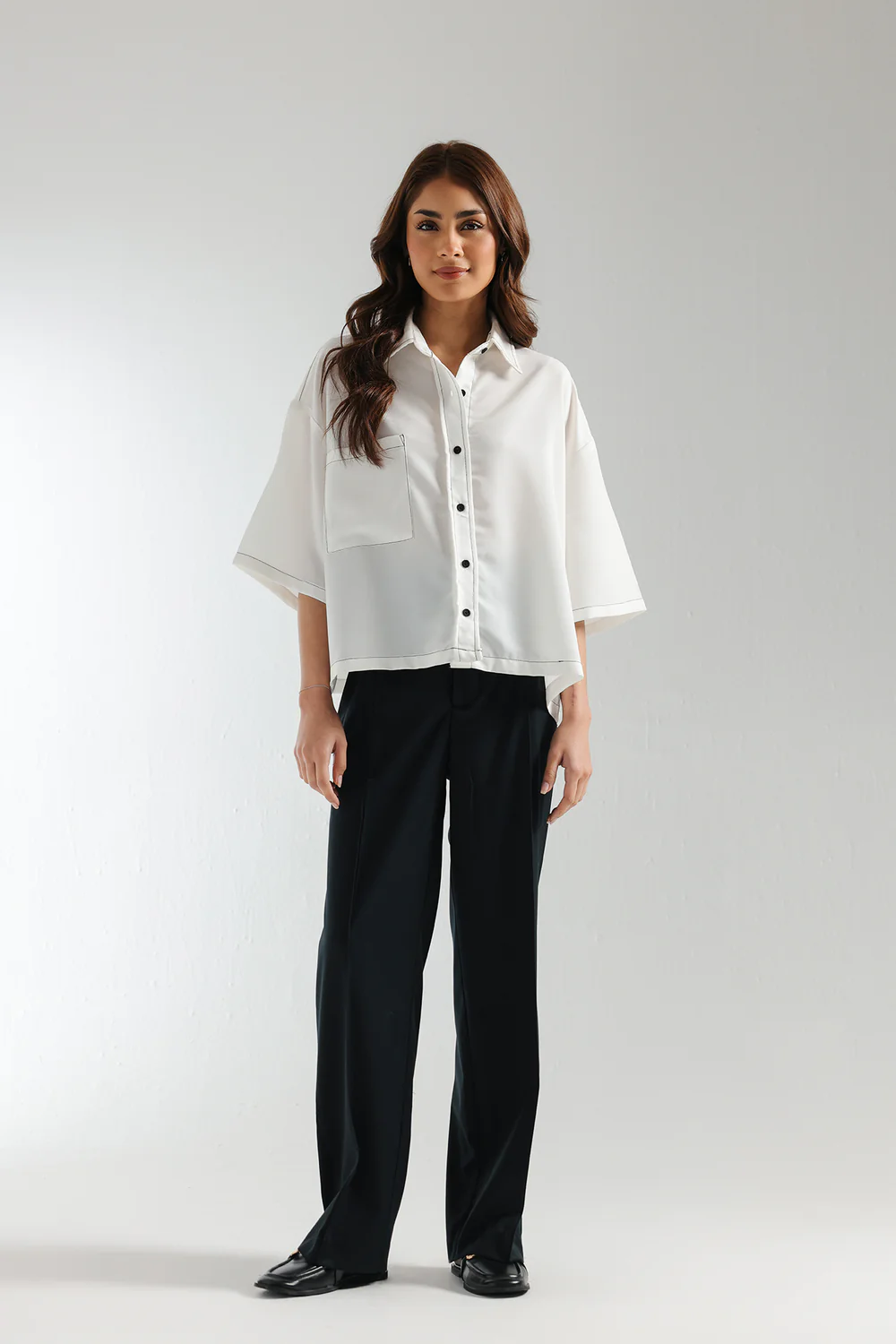 Front studio portrait of Biljiki crisp white boxy button-down shirt with black contrast stitching on a 5'6 model.