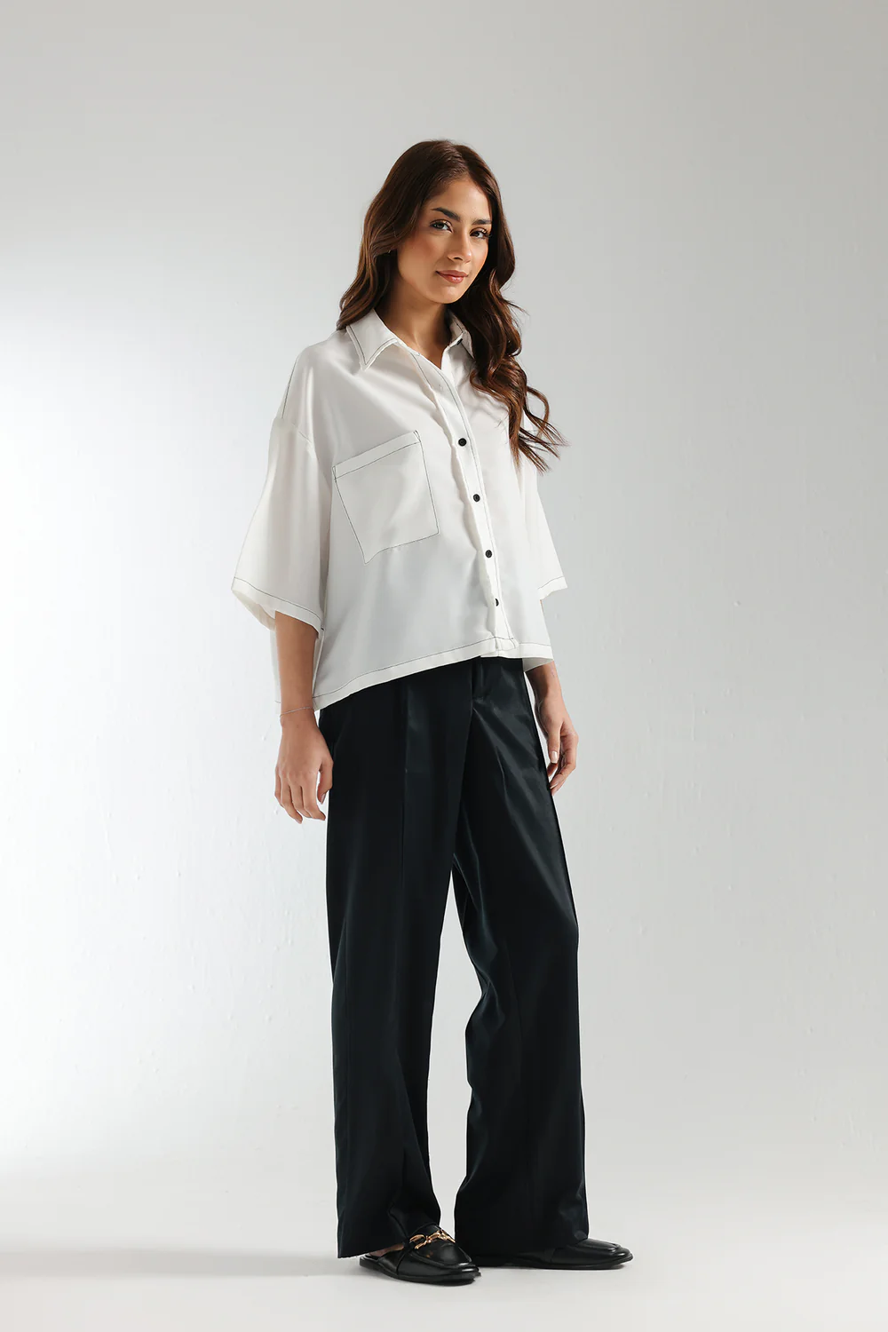 Side studio portrait of Biljiki crisp white boxy button-down shirt with black contrast stitching on a 5'6 model.