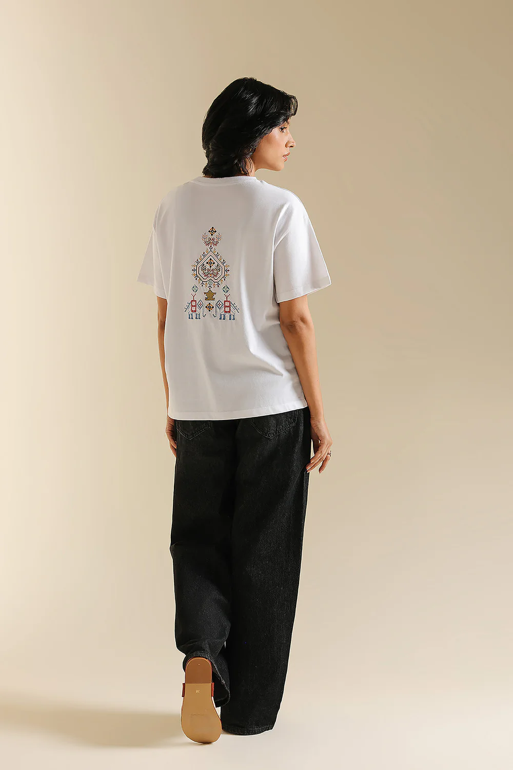 Back studio portrait of Biljiki crisp white t-shirt featuring multi-colored geometric embroidery on a 5'6 model.