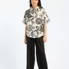 "Model wearing a beige button-down cotton shirt with black floral print and loose-fit black pants"